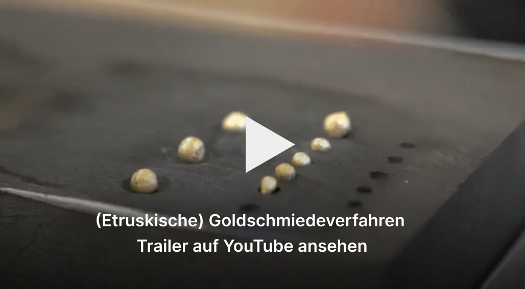 Vorschaubild. Kleine Goldkügelchen auf schwarzer Halterung. Beschriftung: Etruskische Goldkügelchen, Trailer auf YouTube ansehen.